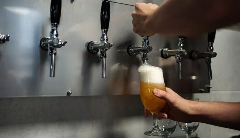 Bartender pours draught beer into a glass beneath a row of taps
