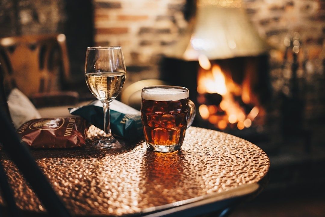 Pint and wine glass on a pub table beside a glowing fireplace